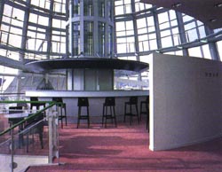 ガラス張りの壁の内側に円形にテーブルと椅子が設置されている写真