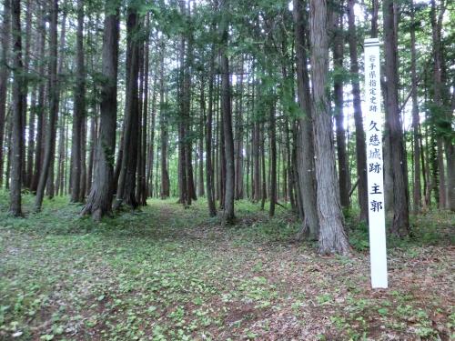 「久慈城跡 主郭」と立札のある木々がたくさん生えている土地の写真