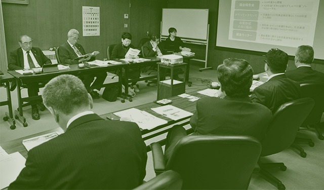 全体を緑に加工されたホワイトボードのある会議室で議論している写真