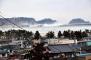 住宅街の奥でしぶきをあげる海の写真