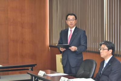 着席したスーツ姿の男性の横に立ち資料を持っているスーツ姿の男性の写真