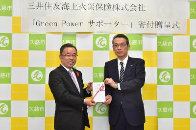 「三井住友海上火災保険株式会社 「Green Power サポーター」寄付贈呈式」と書かれた横断幕を背に、のし袋を一緒に持つスーツ姿の男性2名の写真