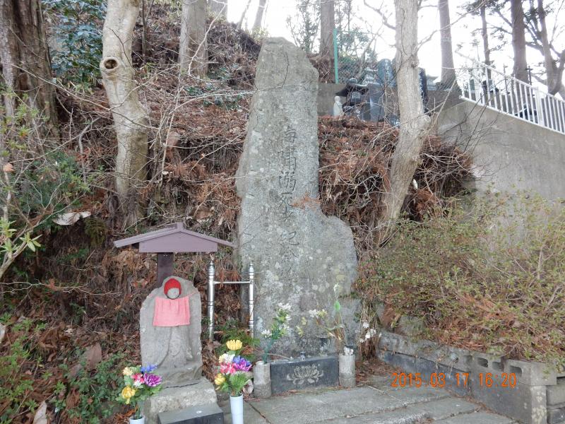 花が供えられた小さな地蔵の横に立つ石碑の写真