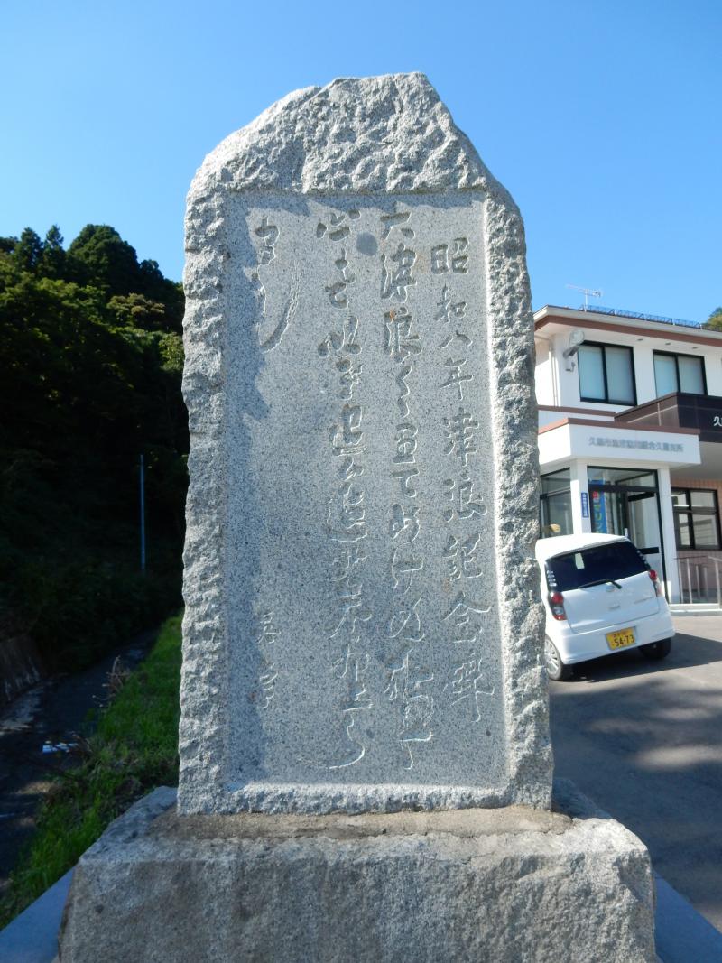 二階建ての建物の前に置かれた薄いグレー色をした石碑の写真