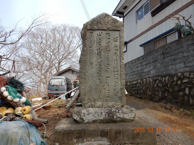 古木や家屋の傍に立つ文字が彫られた石碑の写真