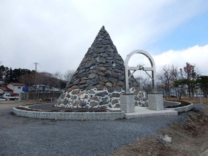 広場の中に立つ、石が連なってできている円錐形のモニュメントの写真