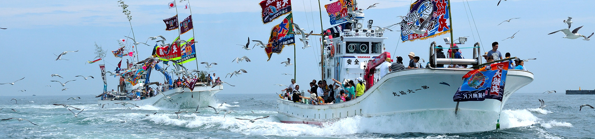 様々な旗を掲げた船が2隻多くの人を乗せて海を進んでいる写真